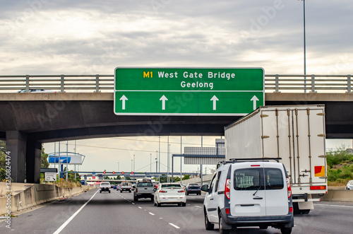 фотографія Traffic flows beneath a directional sign on Melbourne's West Gate Bridge approach, showing exit information for the major arterial route