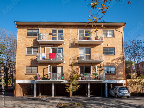 A classic three-story brick apartment building with balconiesl and a ground-floor parking garage. A symmetrical design typical of mid-century Australian residential complex.