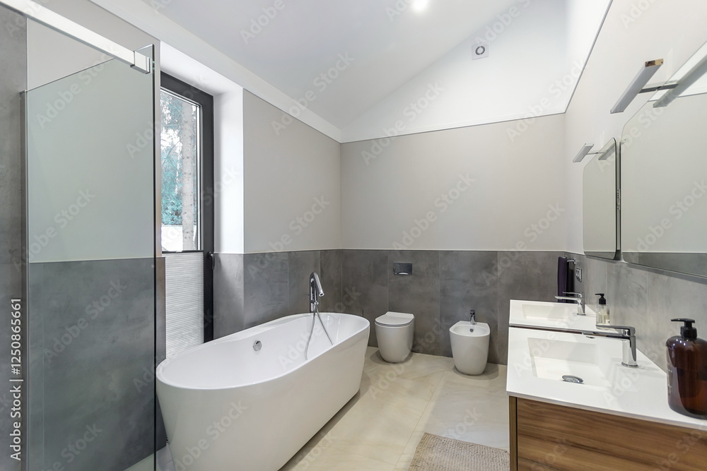 The interior of a bathroom with a window in a private house. The decor is made in light gray tones. The interior of a bathroom with a window in a private house. The decor is made in light gray tones.