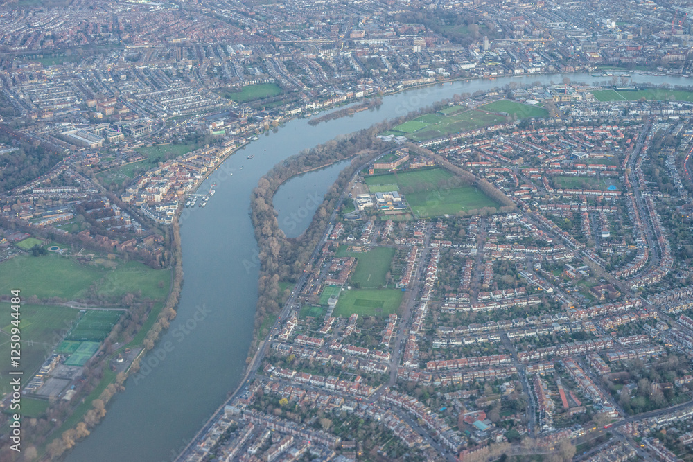 Aerial view of London outskirts suburbs through early morning clouds with Thames river flowing at golden hour sunrise near industrial area