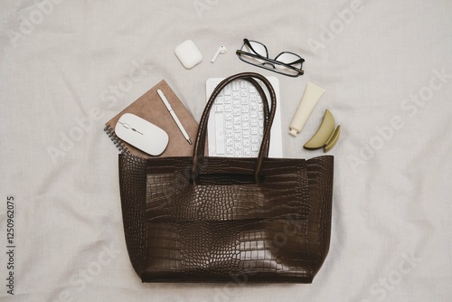 Konstfotografi A stylish and chic brown tote bag that is filled with all the essential items you need for work and daily activities of woman - notebooks, keyboard, glasses, pen, headphones, handcream