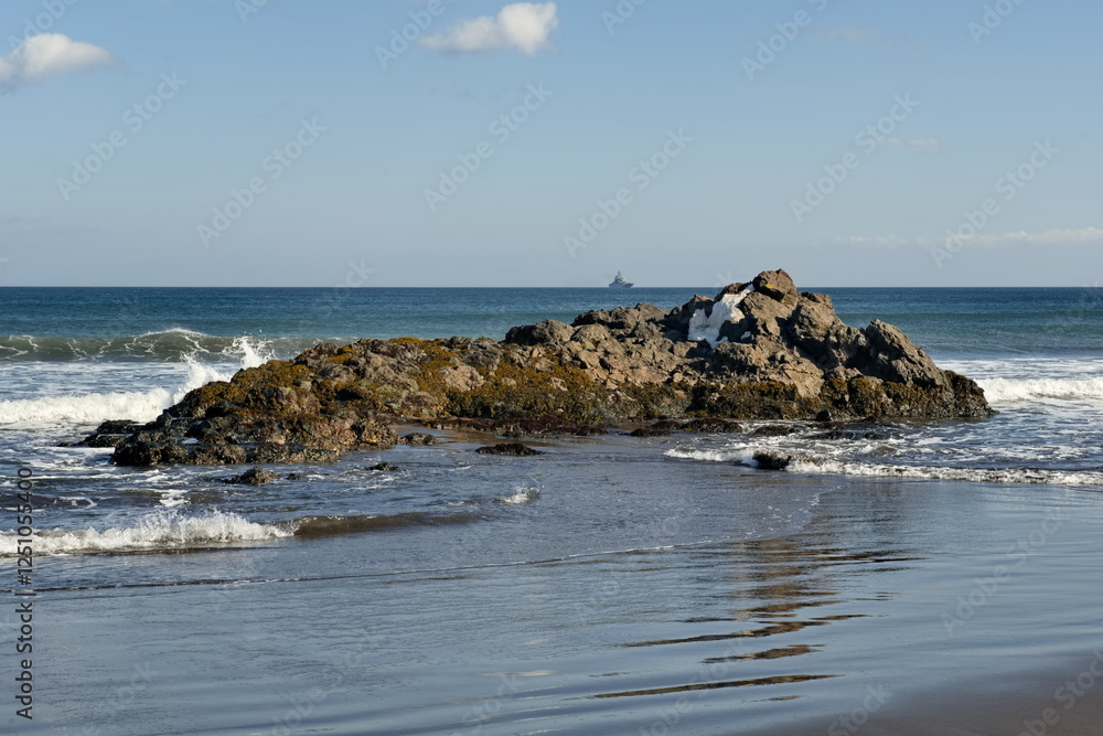 Russia. The Far East. The Kuril Islands. View of the basalt rock outcrops of volcanic origin on the sea sandy shore of Iturup island. Russia. The Far East. The Kuril Islands. View of the basalt rock outcrops of volcanic origin on the sea sandy shore of Iturup island.