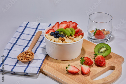 A vibrant and healthy smoothie bowl topped with fresh strawberries, blueberries, kiwi, banana slices, almonds, and pistachio. Placed on a paper cup.