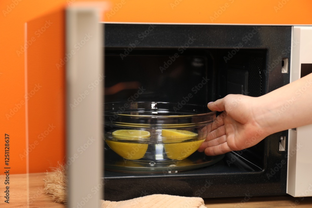 Φωτογραφία Woman putting bowl with water and lemon into microwave oven at table indoors, cl