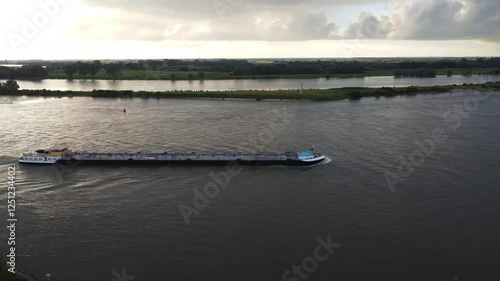 Wallpaper Mural A cargo ship transports containers along a serene river during the golden hour. The water reflects the vibrant colors of the sky, creating a peaceful atmosphere. Torontodigital.ca
