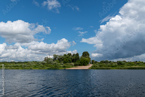 view of the road ending in a river in summer with blue sky and white clouds