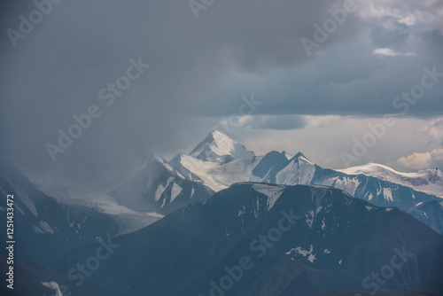 Dark atmospheric landscape with mountain silhouettes and large snow-capped pe...