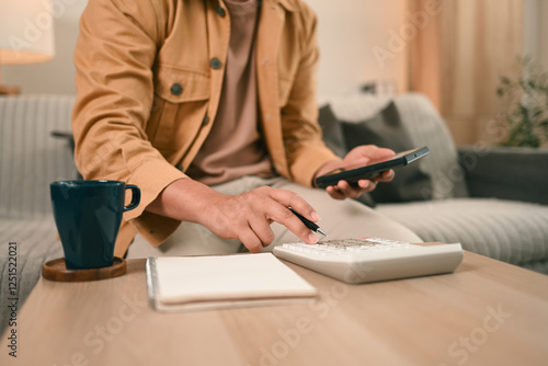 A Close-up of a man in a casual outfit calculates expenses using a calculator, Taking control of personal finances at home