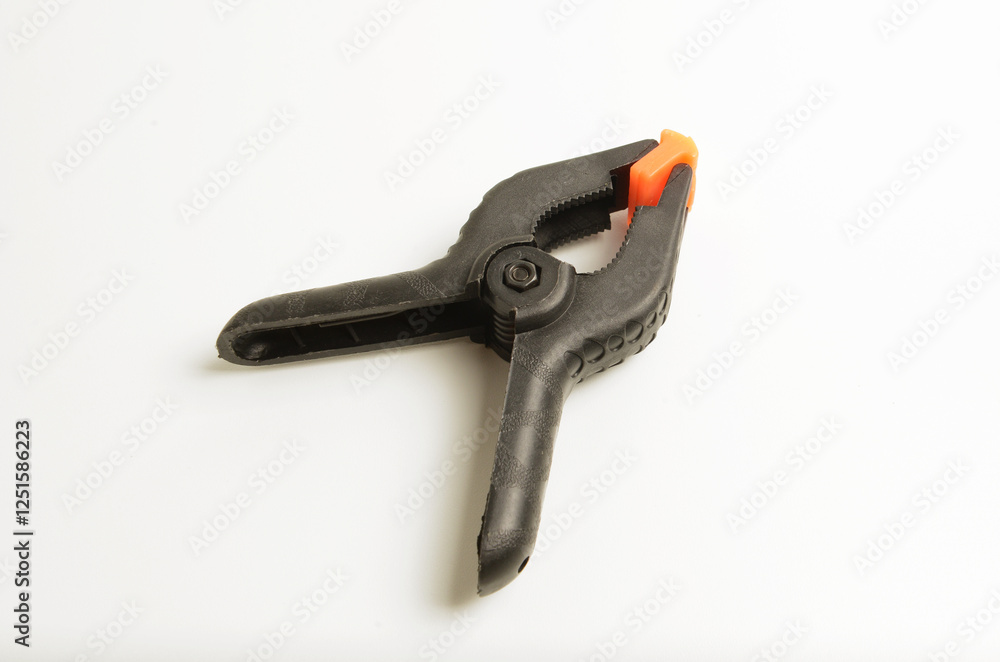 Close-up of a black plastic spring clamp with orange tips, commonly used to clamp paper, photo and backdrops for photography. Close-up of a black plastic spring clamp with orange tips, commonly used to clamp paper, photo and backdrops for photography.