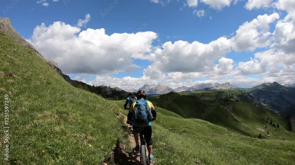 A biker navigates a narrow ridge trail surrounded by sweeping views of the Dolomite peaks and verdant alpine pastures. A biker navigates a narrow ridge trail surrounded by sweeping views of the Dolomite peaks and verdant alpine pastures.