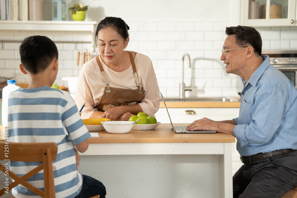 Asian grandmother watching and talking with grandson while doing homework and grandfather working with laptop at the counter kitchen on morning weekend. Family care enjoy living together Asian grandmother watching and talking with grandson while doing homework and grandfather working with laptop at the counter kitchen on morning weekend. Family care enjoy living together
