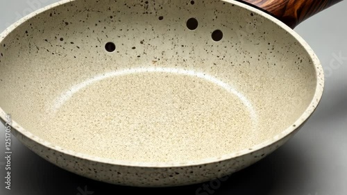 Stylish speckled frying pan with wooden handle on a neutral background