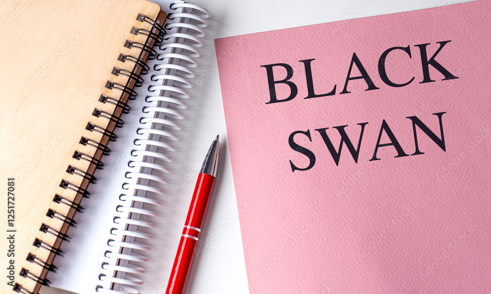 Black swan text on a pink notebook with spiral notepads and a red pen on a white background