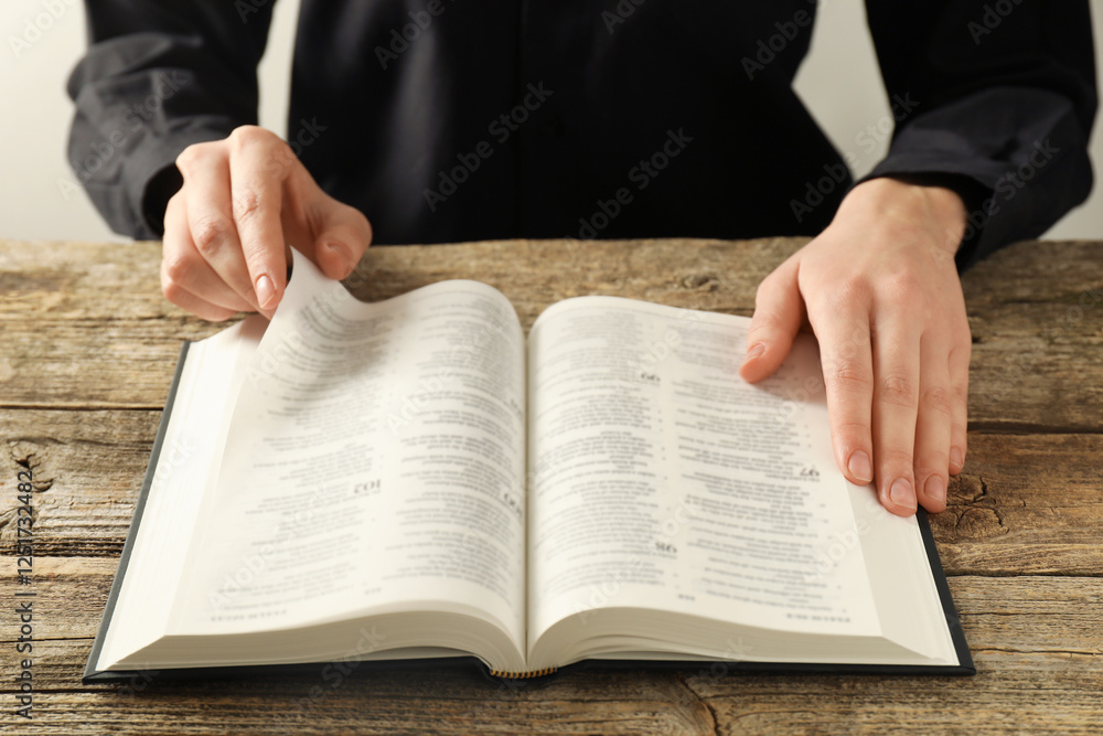 Fototapeta premium Woman reading Holy Bible in English language at wooden table, closeup