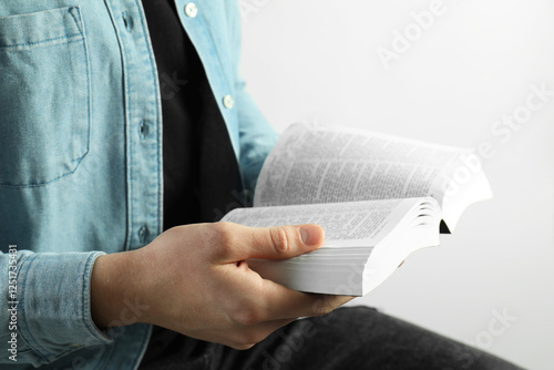 Man reading Holy Bible on light background, closeup photo