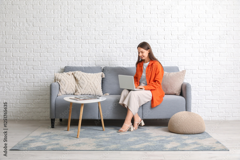 Obraz premium Young pretty woman chatting with laptop on grey sofa at home