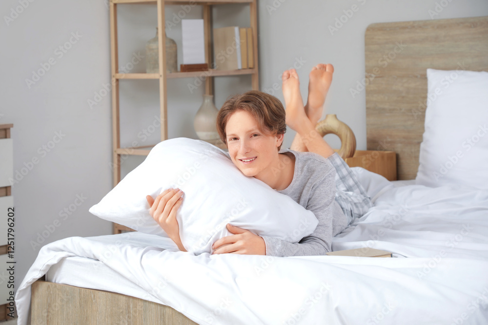 Handsome young happy man in pajamas with pillow and book lying on bed at home Handsome young happy man in pajamas with pillow and book lying on bed at home