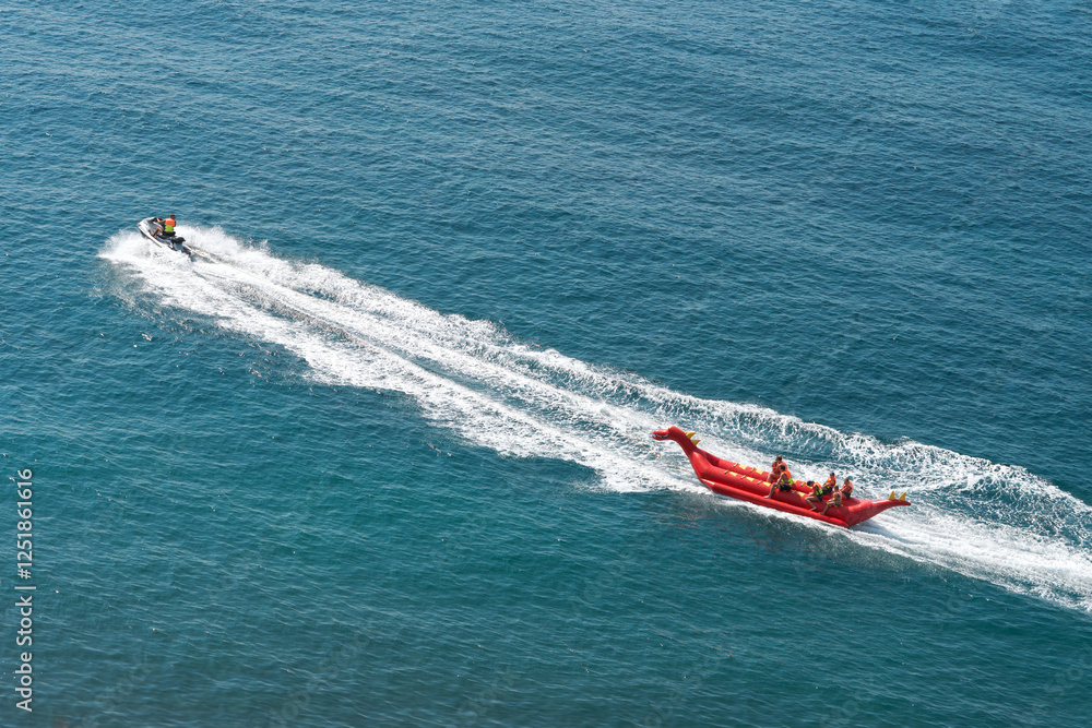 Fototapeta premium Sea ride. A group of tourists riding an inflatable watercraft pulling an aquabike at speed. Copy space.