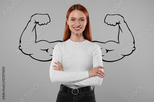 Konstfotografi Confident beautiful woman with drawing of strong arms behind her on grey backgro