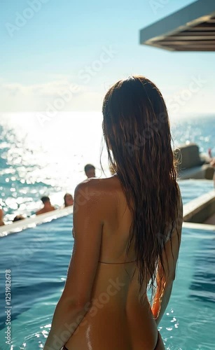 Young Caucasian woman in a white bikini sipping a cocktail at a luxurious hotel pool in summertime		