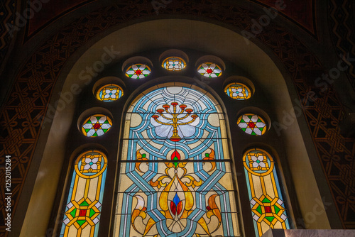 Close-up shot of a stained glass window featuring a menorah at the center, surrounded by colorful geometric patterns and set within an arched frame photo