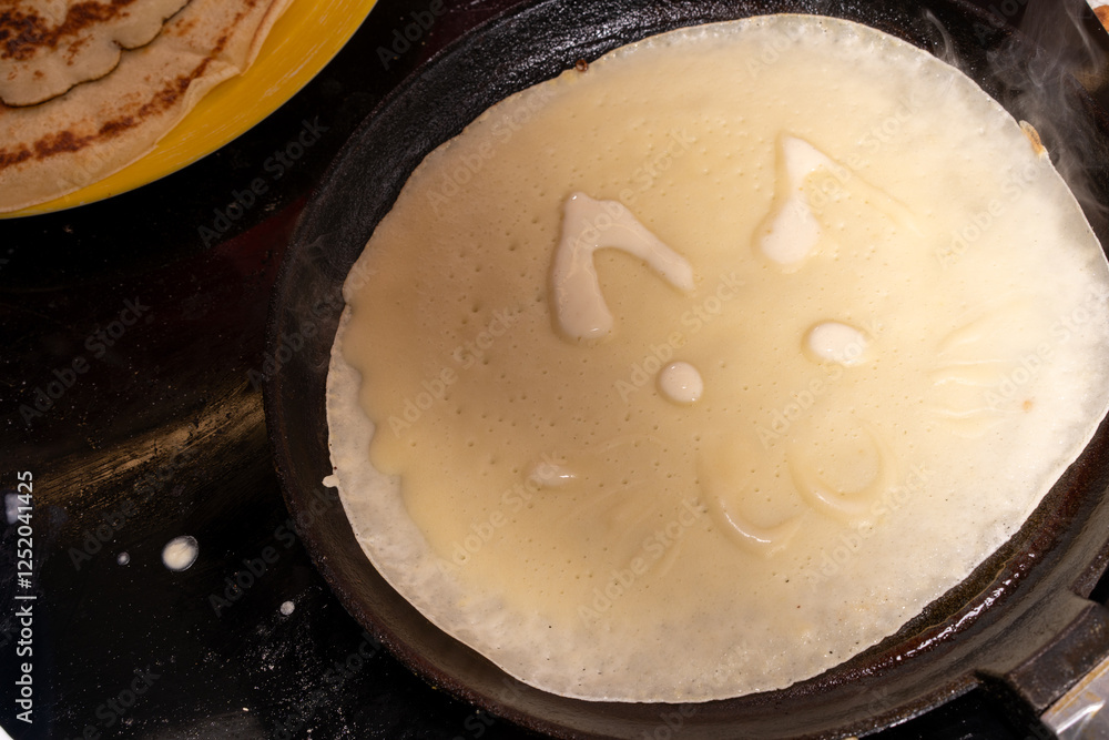Creative crepe in a pan resembling a cat's face, with ears, eyes, nose, and whiskers.