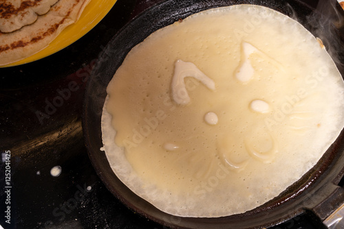 Creative crepe in a pan resembling a cat's face, with ears, eyes, nose, and whiskers.