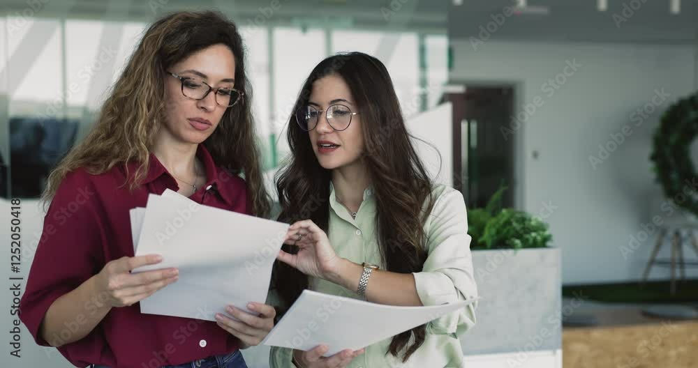 Female colleagues reviewing papers in office, engaged in teamwork or brainstorming session, learning written data in report, budgeting or planning, development strategy based on received information