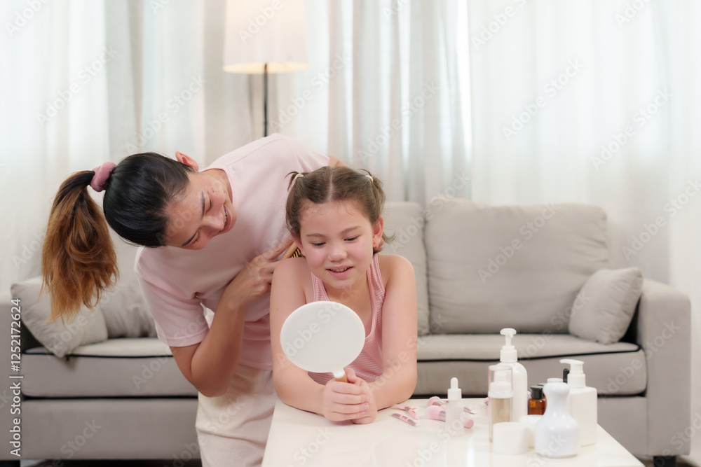 Caucasian girl learning makeup. An Asian woman gently brushes the hair of a young Caucasian girl as she looks at herself in the mirror. A warm family bonding moment filled with love and care. Caucasian girl learning makeup. An Asian woman gently brushes the hair of a young Caucasian girl as she looks at herself in the mirror. A warm family bonding moment filled with love and care.