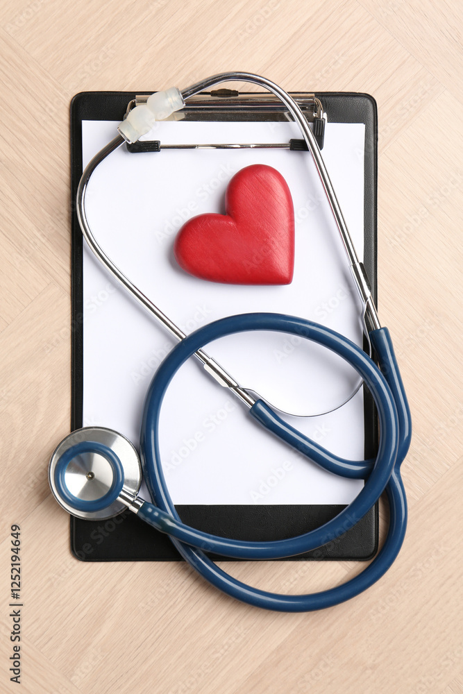 Cardiology. Clipboard, stethoscope and red decorative heart on wooden table, top view Cardiology. Clipboard, stethoscope and red decorative heart on wooden table, top view