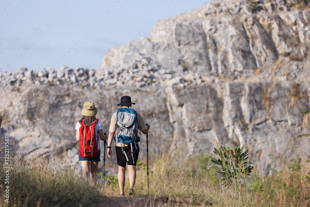 A couple hikes along a scenic mountain trail, carrying backpacks and trekking poles. A couple hikes along a scenic mountain trail, carrying backpacks and trekking poles.