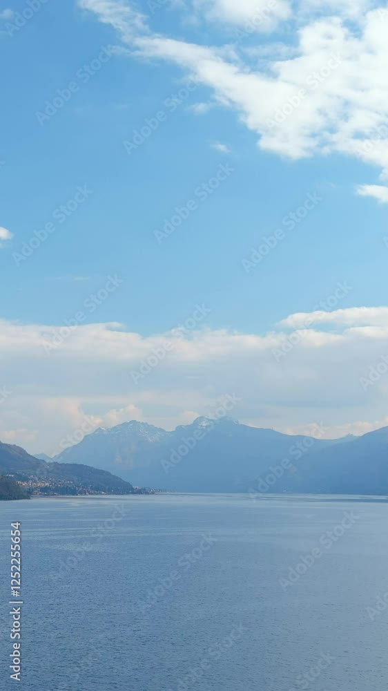 Lago di Como. Aerial vertical view of great lake Como waters, vicinity of Varenna. Fresh air, clouds along the horizon, mountain skyline, picturesque fishing villages. Famous tourist region. Italy Lago di Como. Aerial vertical view of great lake Como waters, vicinity of Varenna. Fresh air, clouds along the horizon, mountain skyline, picturesque fishing villages. Famous tourist region. Italy