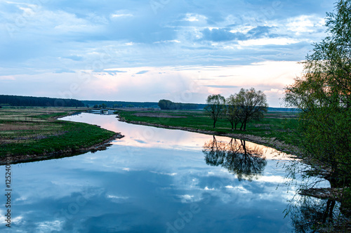 A serene view of the Tiasmyn River in Ukraine, reflecting the tranquil sky and lush greenery as twilight colors the horizon with soft hues. photo