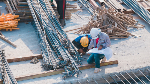 Construction Workers Collaborating on Site, Two construction workers review blueprints amidst piles of materials on construction site, ensuring accurate project planning and execution photo