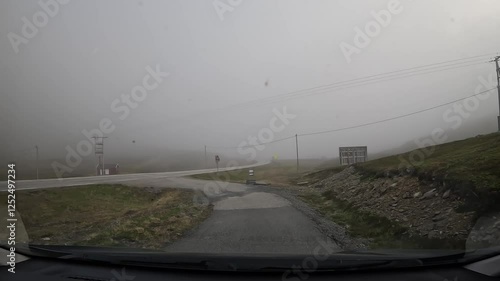 Driving through the tundra in northern Norway. The road is surrounded by grassy hills and rocks. Several traffic signs and a barrier are visible.