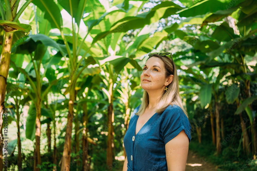 A young woman walking along a tropical path surrounded by banana trees A young woman walking along a tropical path surrounded by banana trees