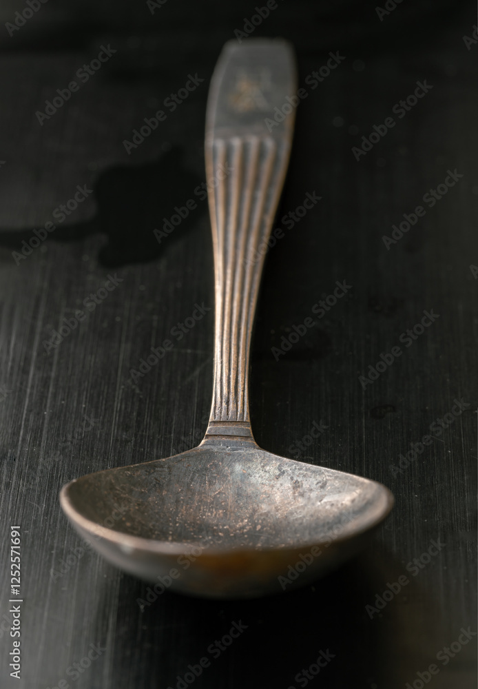 Perspective surface view of Ancient vintage spoon isolated on black background. Close-up of Black worn metal vintage spoon in dark tone, Highlighting its texture and design, use it as your Copy space.