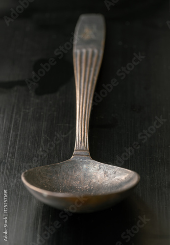 Obraz na płótnie Perspective surface view of Ancient vintage spoon isolated on black background. Close-up of Black worn metal vintage spoon in dark tone, Highlighting its texture and design, use it as your Copy space. w salonie