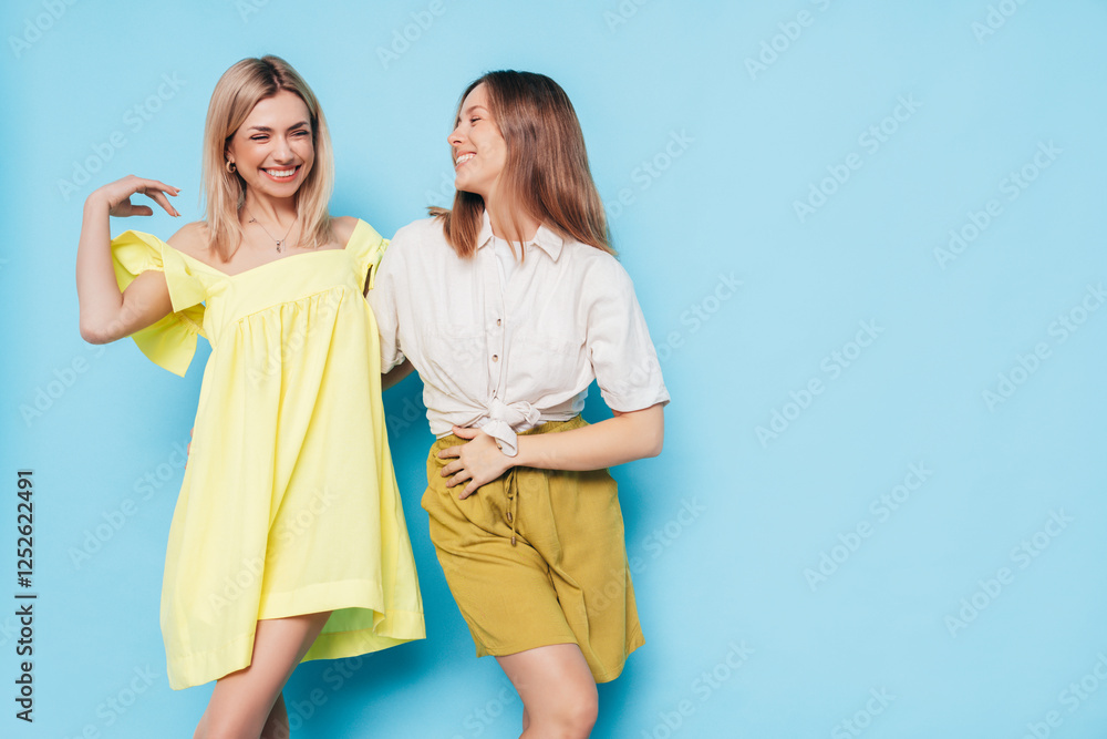 Two young beautiful smiling brunette and blond hipster female in trendy summer clothes. Lovely women posing on blue background in studio. Positive models having fun. Cheerful and happy. isolated Two young beautiful smiling brunette and blond hipster female in trendy summer clothes. Lovely women posing on blue background in studio. Positive models having fun. Cheerful and happy. isolated