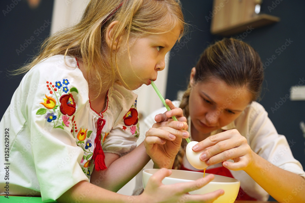 Mother and daughter at the table in traditional Ukrainian costumes painting eggs for Easter Mother and daughter at the table in traditional Ukrainian costumes painting eggs for Easter
