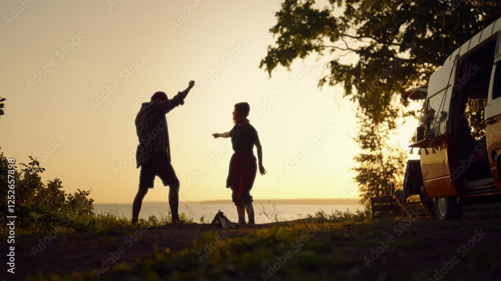 Travel by camper van, silhouette of two carefree campers dancing on lake shore. Motorhome trip in beautiful location, escape from city, people enjoying freedom, calmness and solitude, slow motion Travel by camper van, silhouette of two carefree campers dancing on lake shore. Motorhome trip in beautiful location, escape from city, people enjoying freedom, calmness and solitude, slow motion