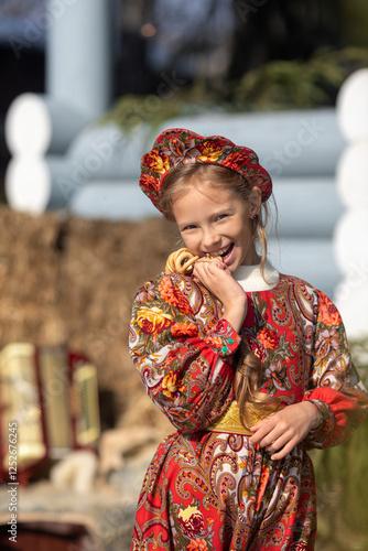 A blonde girl in a national Russian costume on the Maslenitsa holiday. A beautiful russian girl in a national costume made of a fur cape and kokoshnik on the background of a hayloft. 