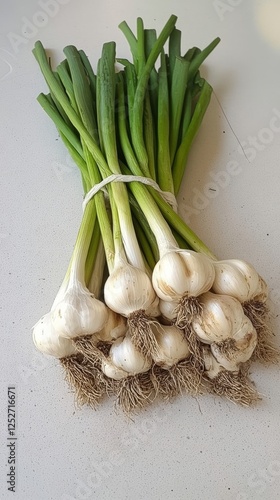 Fresh garlic bulbs with green stems gathered on a kitchen countertop for cook...