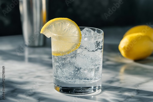 Refreshing drink with lemon slice and ice on a marble counter in bright light