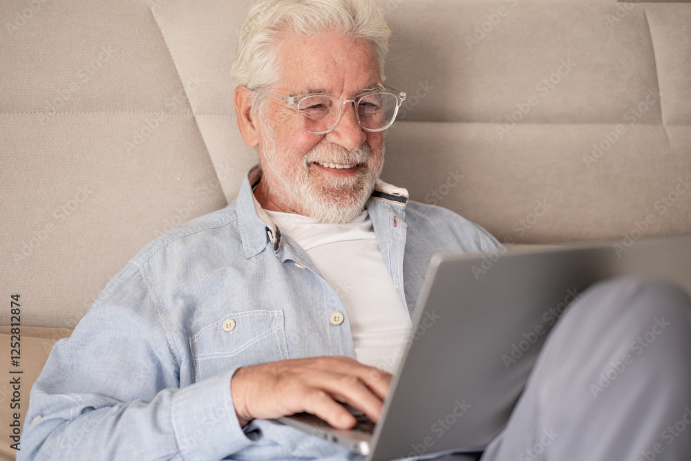 Smiling handsome caucasian senior bearded man with eyeglasses lying on bed using computer, elderly retiree browsing internet by laptop Smiling handsome caucasian senior bearded man with eyeglasses lying on bed using computer, elderly retiree browsing internet by laptop