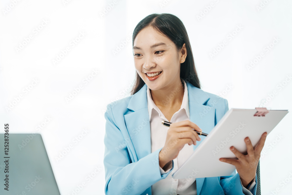 An Asian female accountant works happily at her desk in the office, using a laptop to analyze financial charts. She manages business finance and online transactions for company success An Asian female accountant works happily at her desk in the office, using a laptop to analyze financial charts. She manages business finance and online transactions for company success