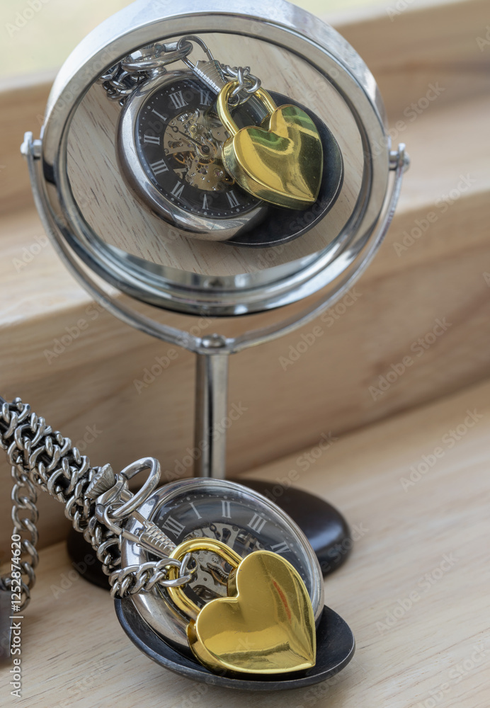 Golden heart shaped love padlock lap over A retro pocket watch with reflection in a round mirror on wooden desk. Love can endure beyond the limitations of time, Concept of Love that transcends time,.