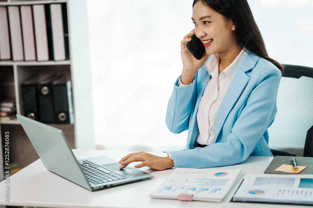 An Asian female accountant works happily at her desk in the office, using a laptop to analyze financial charts. She manages business finance and online transactions for company success An Asian female accountant works happily at her desk in the office, using a laptop to analyze financial charts. She manages business finance and online transactions for company success