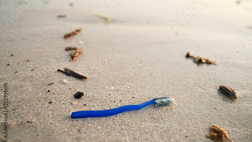 Fotografija A discarded toothbrush on a beach with sea in background, plastic waste in natur