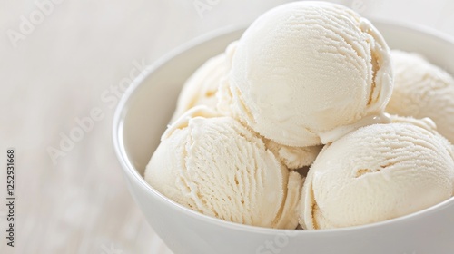 Creamy vanilla ice cream scoops in a white bowl on a light wooden table